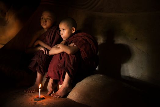 Young novice monks lighting up candle light inside a Buddhist temple, Bagan, Myanmar.