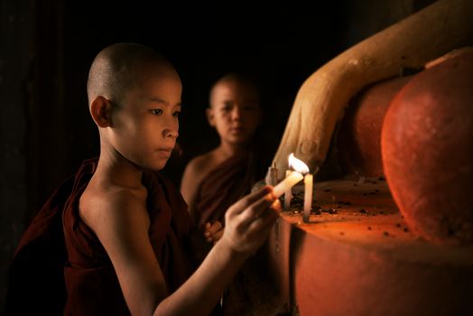Portrait of young novice monks lighting up candlelight inside a Buddhist temple, low light setting, Bagan, Myanmar.