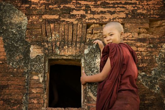 Young novice monk standing outside Buddhist temple, Bagan, Myanmar.