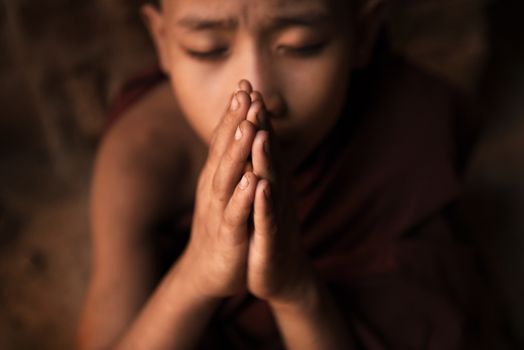 Young novice monk praying inside Buddhist temple, low light with noise setting, Bagan, Myanmar.