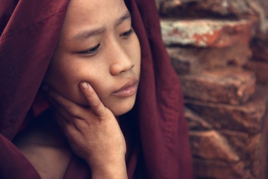 Portrait of young novice monk inside Buddhist temple, low light with noise setting, Bagan, Myanmar.