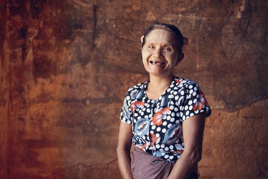 Portrait of traditional old Asian Burmese woman smiling, standing inside a temple, low light, Bagan, Myanmar