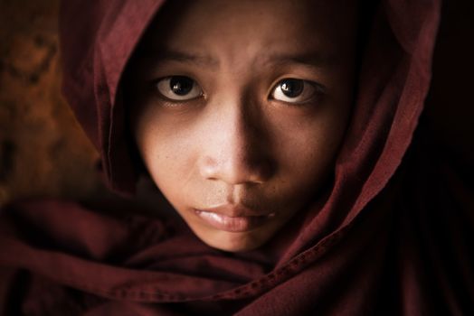 Close up face of  young novice monk covered with robe, low light with noise setting, Bagan, Myanmar.