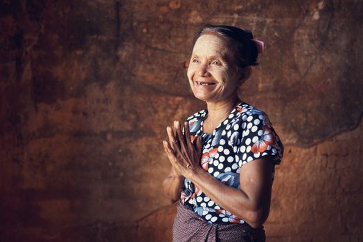 Portrait of traditional Asian Burmese woman greeting, standing inside a temple, low light, Bagan, Myanmar