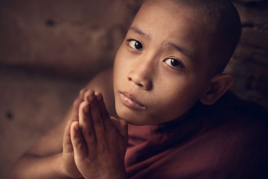 Portrait of young novice monk praying inside Buddhist temple, low light with noise setting, Bagan, Myanmar.