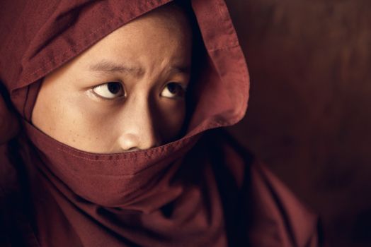 Portrait of young novice monk inside Buddhist temple, low light with noise setting, Bagan, Myanmar.