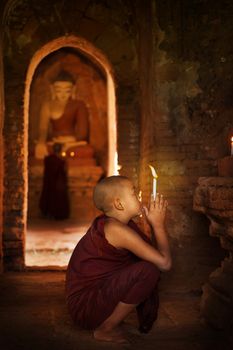 Portrait of young novice monks praying with candlelight inside a Buddhist temple, Bagan, Myanmar.
