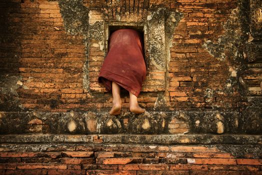 Young novice monks climbing into Buddhist temple from window, Bagan, Myanmar.