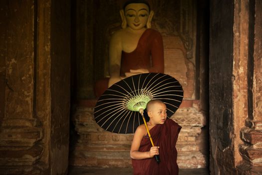 Portrait of young novice monks with umbrella inside ancient Buddhist temple, Bagan, Myanmar.