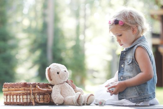 Pretty girl playing with teddy bear outdoors