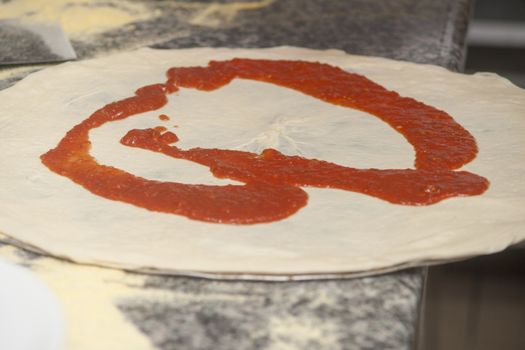 Man chef with raw pizza. Young male in uniform preparing pizza on table.