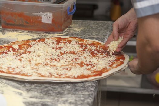 Man chef with raw pizza. Young male in uniform preparing pizza on table.