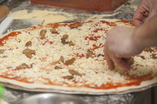 Man chef with raw pizza. Young male in uniform preparing pizza on table.