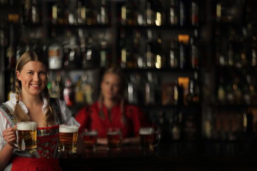 Pretty oktoberfest blonde woman holding beer mugs in bar