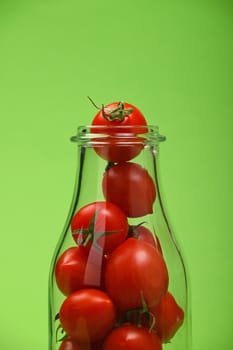 Big glass bottle full of red cherry tomatoes over green background as symbol of fresh natural organic juice or ketchup, close up crop