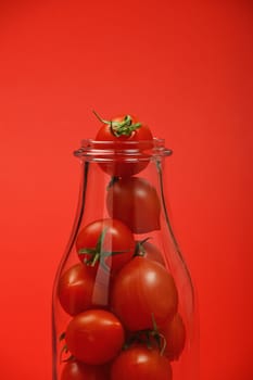 Big glass bottle full of cherry tomatoes over red background as symbol of fresh natural organic juice or ketchup, close up crop