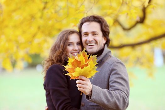 Smiling couple with bunch of leaves hugging over autumn natural background