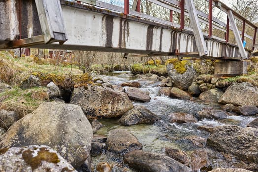 A rocky steam under a bridge in forest.