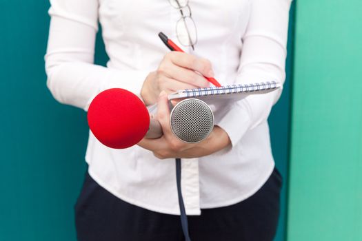 Female journalist or reporter at press conference, taking notes, holding microphones