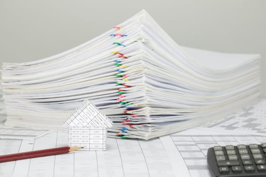 House and pencil on finance account have blur pile overload paperwork of report and receipt with colorful paperclip and calculator place on white background.