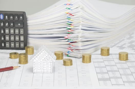 House on finance account have blur pencil and pile of gold coins with calculator place vertical and pile overload paperwork of report and receipt with colorful paperclip on white background.