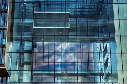 Artistic work of my own.  Intentional blur; Photoshop editing.
Modern blue glass wall of an office building in the background a storm with lightning.