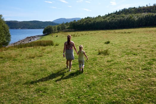 Mother and daughter holding hands in a grassy green field.