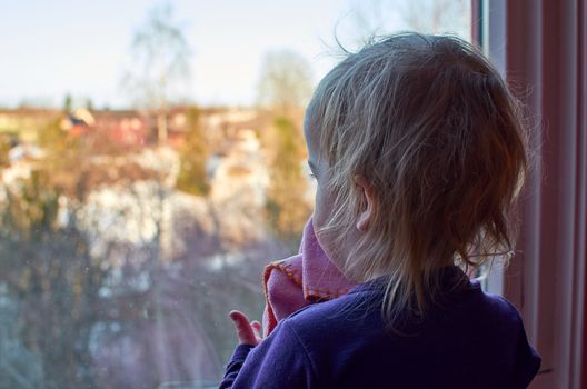Young girl with blanket looking out of a window.