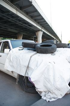 Old dirty abandoned car with tires under bridge in city