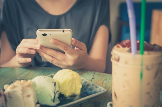 Afternoon scene of young woman using smartphone for social networking in ice cream cafe on weekend. Modern lifestyle with technology concept. processed with vintage filter effect