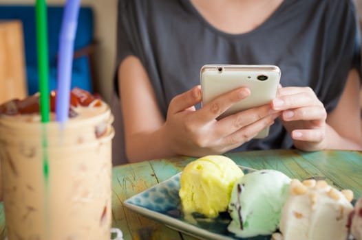 Afternoon scene of young woman using smartphone for social networking in ice cream cafe on weekend. Modern lifestyle with technology concept.