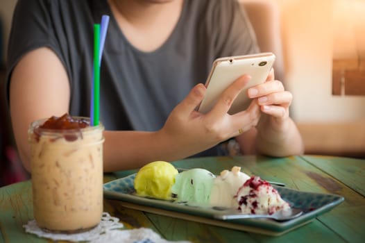 Afternoon scene of young woman using smartphone for social networking in ice cream cafe on weekend. Trendy lifestyle concept with communication technology.