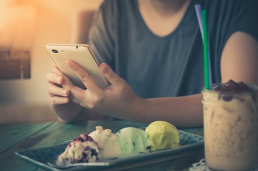 Afternoon scene of young woman using smartphone for social networking in ice cream cafe on weekend. Trendy lifestyle concept with communication technology.