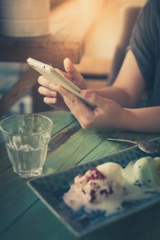 Afternoon scene of young woman using smartphone for social networking in ice cream cafe on weekend. Modern lifestyle with technology concept. processed with vintage filter effect