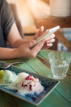 Afternoon scene of young woman using smartphone for social networking in ice cream cafe on weekend. Modern lifestyle with technology concept.