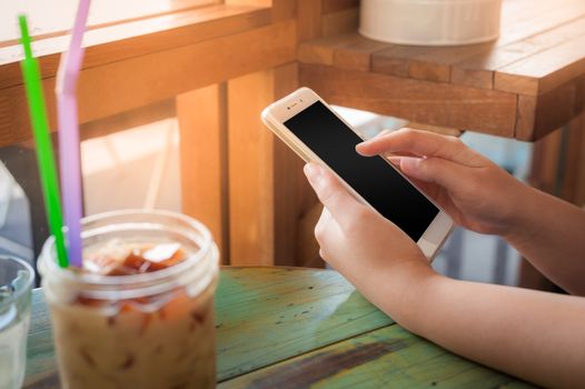 Woman hand holding smartphone on wood table in cafe on weekend afternoon. Trendy lifestyle concept with communication technology.