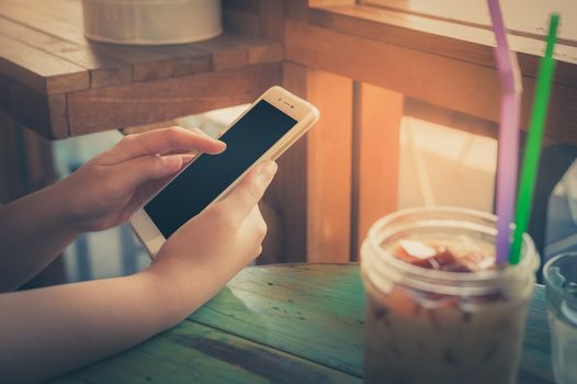 Woman hand holding smartphone on wood table in cafe on weekend afternoon. Trendy lifestyle concept with communication technology. processed with vintage filter effect