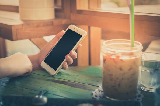 Woman hand holding smartphone on wood table in cafe on weekend afternoon. Trendy lifestyle concept with communication technology. processed with vintage filter effect