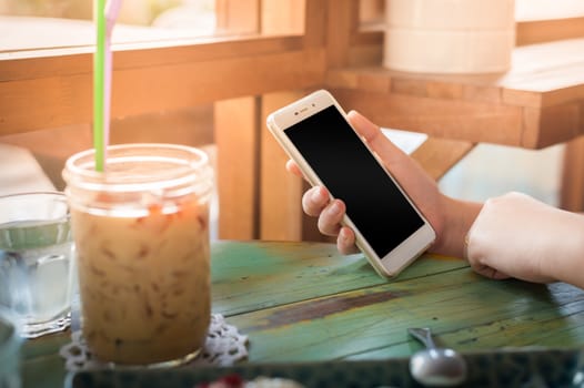Woman hand holding smartphone on wood table in cafe on weekend afternoon. Trendy lifestyle concept with communication technology.