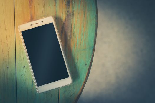 Smartphone with blank area on touch screen on wood table in afternoon time at cafe. Trendy lifestyle concept with vintage filter effect