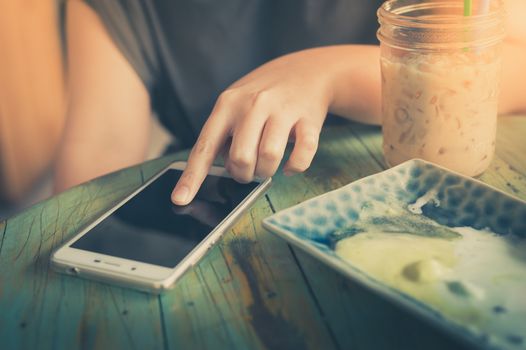 Woman hand touching on smartphone screen in cafe on weekend afternoon. Trendy lifestyle concept with technology with vintage filter effect