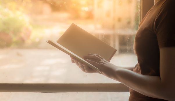 Young woman reading blank book beside window in morning time on weekend. Weekend lifestyle concept