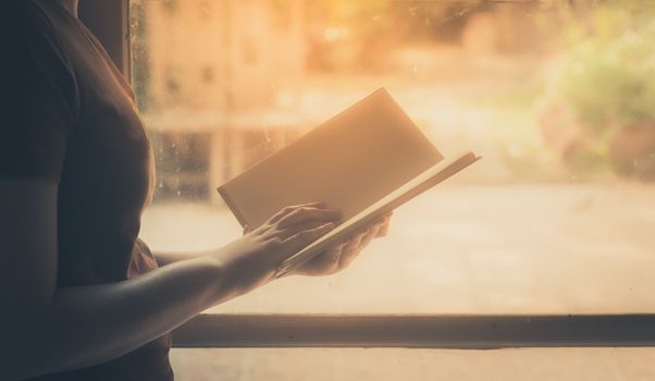 Young woman reading blank book beside window in morning time on weekend. Weekend lifestyle concept with instagram vintage filter effect