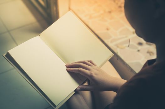 Young woman reading blank book while sitting beside window in morning time on weekend. Morning lifestyle on weekend concept with vintage filter effect