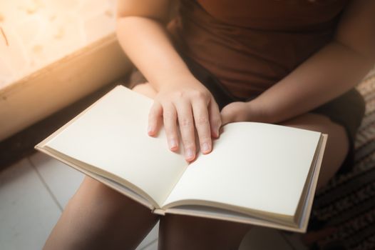 Young woman reading blank book while sitting beside window in morning time on weekend. Morning lifestyle on weekend concept.