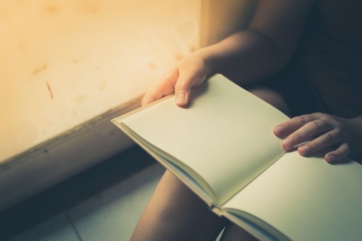 Young woman reading blank book while sitting beside window in morning time on weekend. Morning lifestyle on weekend concept with vintage filter effect
