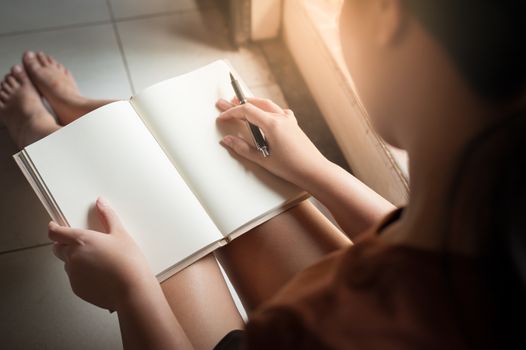 Young woman reading blank book while sitting beside window in morning time on weekend. Morning lifestyle on weekend concept.