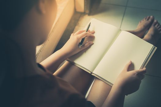 Young woman reading blank book while sitting beside window in morning time on weekend. Morning lifestyle on weekend concept with vintage filter effect