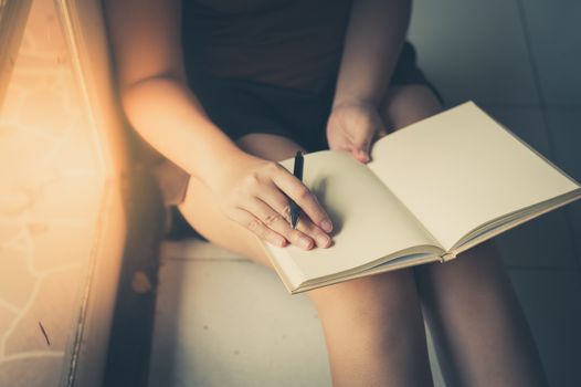 Young woman reading blank book while sitting beside window in morning time on weekend. Morning lifestyle on weekend concept with vintage filter effect