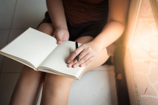 Young woman reading blank book while sitting beside window in morning time on weekend. Morning lifestyle on weekend concept.